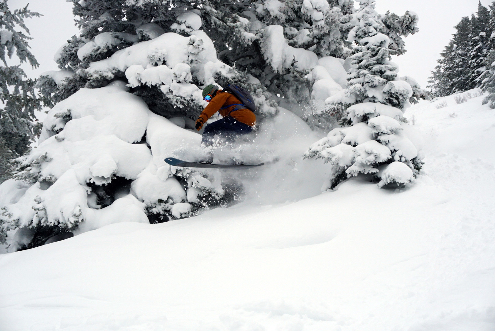Snowboarder airborne past snow covered pine trees