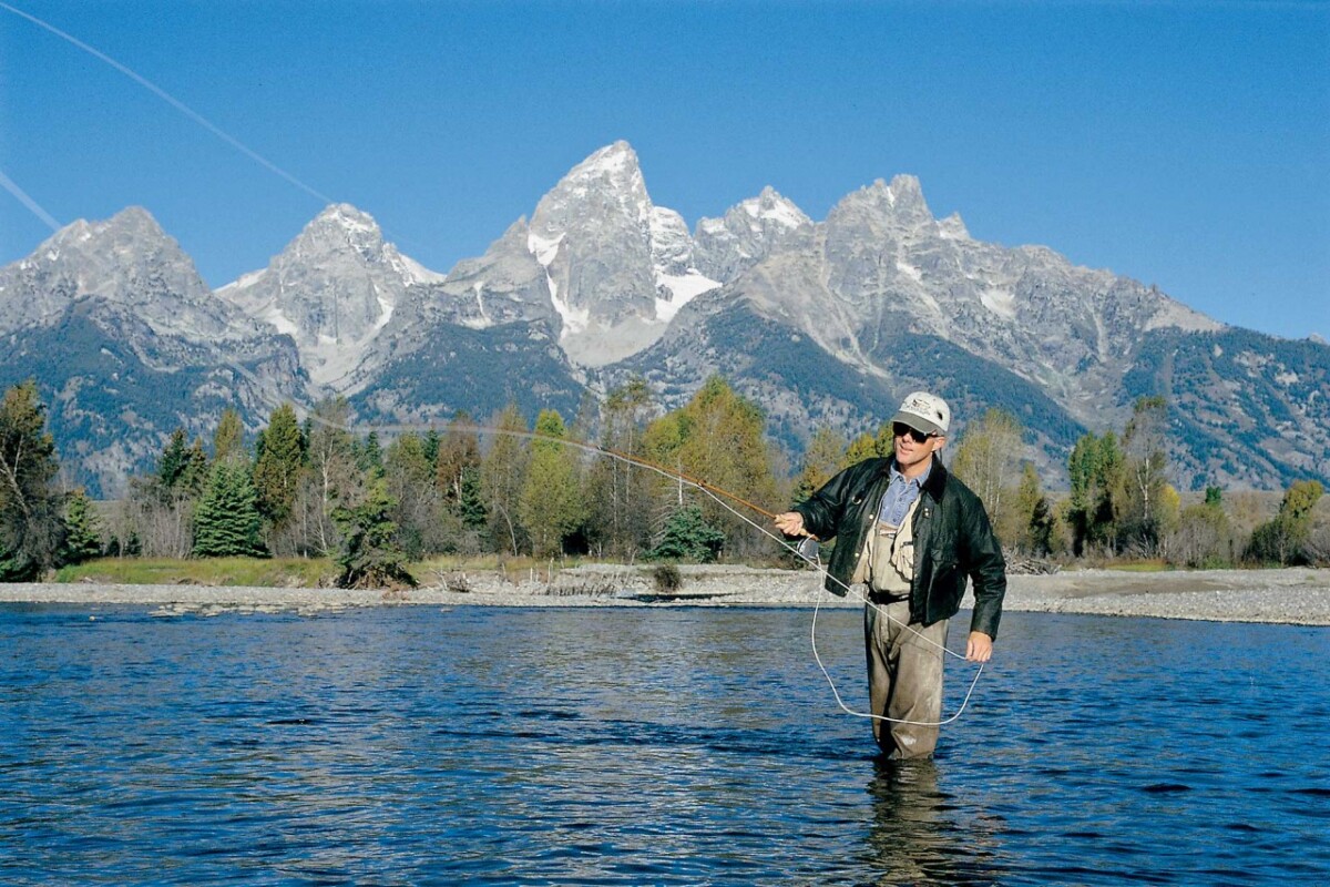 Fly fishing in Jackson Hole in mountain lake with Grand Tetons in background