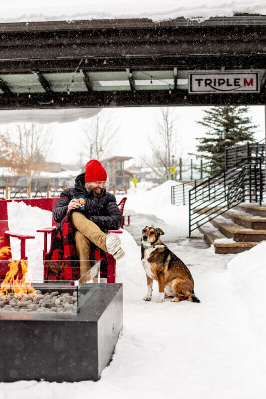 Dog and Man sitting outside Triple M by Fire pit