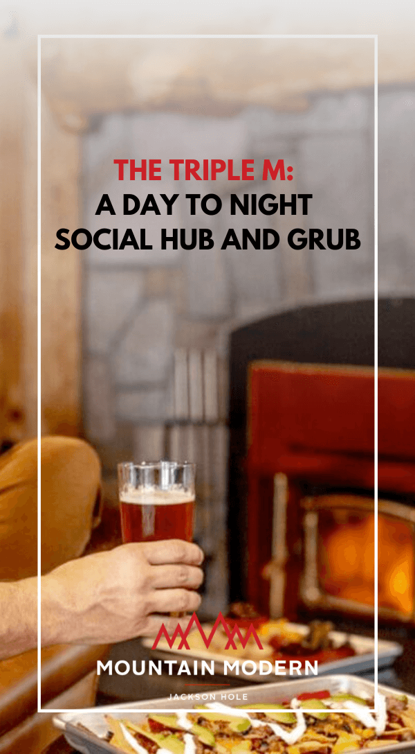 Hand holding a glass of beer over a plate of nachos